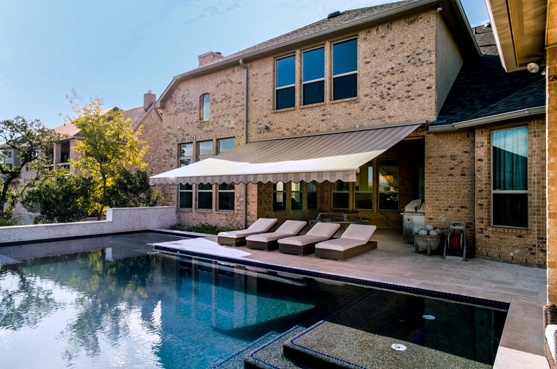 A serene backyard pool with a lounge area shaded by a retractable awning by Sunesta