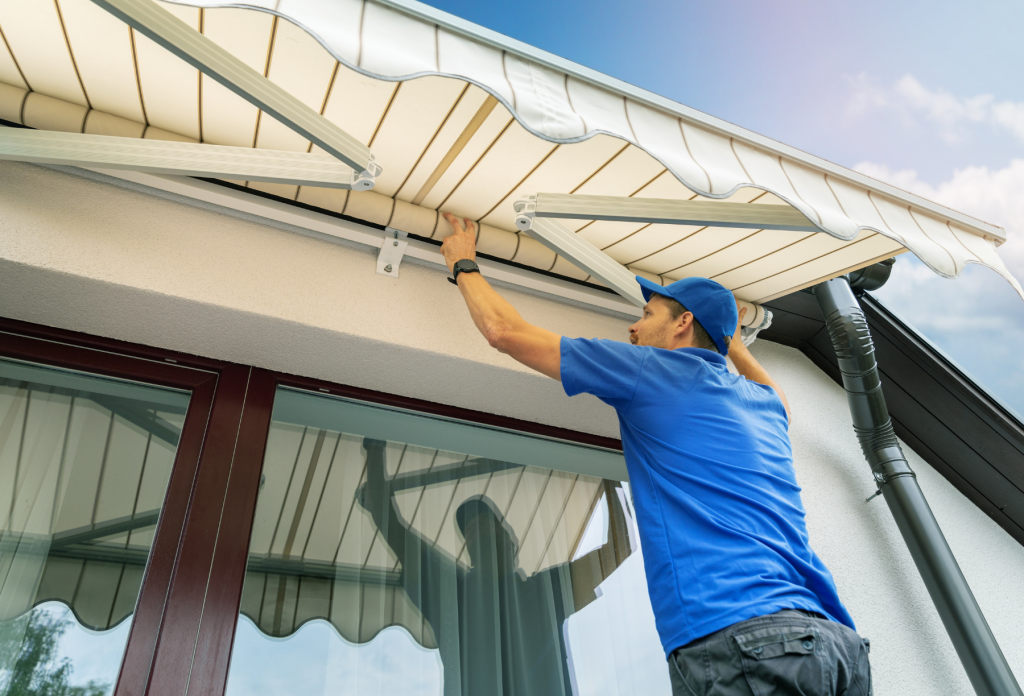 An awning maintenance professional installing a white and gold retractable awning.